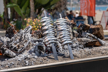 Obraz premium Fresh Sardines Grilling Over Open Flame on Beach – Authentic Coastal Cooking Scene