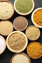 Different superfood powders in bowls on dark textured table, flat lay