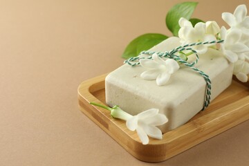 Bar of soap and jasmine flowers on light brown background, closeup. Space for text