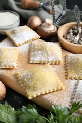 Uncooked ravioli, mushrooms and sauce on black table, closeup