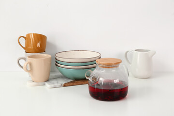 Composition with glass teapot and different kitchen utensils on white table