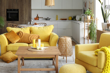 Interior of light open space kitchen with yellow sofa, armchair and wooden coffee table