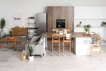 Interior of light open plan kitchen with island table and grey sofas