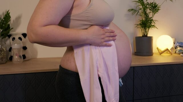 Pregnant woman with big belly in anticipation for the motherhood. Concept of pregnant woman wondering if it a boy or a girl gender with with rompers in hands. Twins