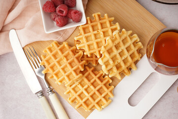 Wooden board of tasty waffles with raspberries and and maple syrup on white background