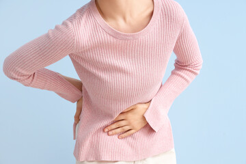 Young woman suffering from stomach ache on blue background, closeup