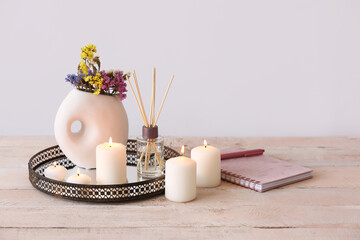 Burning candles, reed diffuser, vase with beautiful flowers and notebook on table near white wall