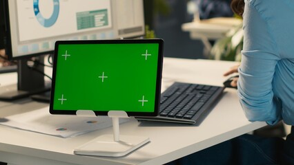 Close up of employee sitting at office desk, using green screen tablet to solve tasks during job shift. Office clerk doing email communication in workplace using chroma key device, camera A