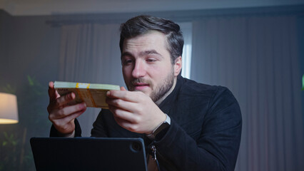 Excited man holding cash in front of laptop