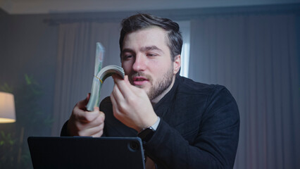 A man sits at a desk holding a stack of dollar bills and two golden coins, talk to the camera, expressing enthusiasm and curiosity about finances. Investment, cryptocurrency, and wealth management