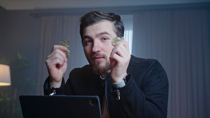 A businessman holds up a stack of cash and mobile phone while speaking to the camera in a professional home office. Investment, cryptocurrency, and wealth management