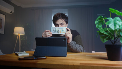 Man holds up a stack of cash while speaking to the camera in a professional home office. Investment, cryptocurrency, and wealth management