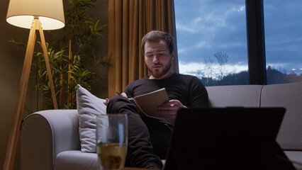 Man reading notebook on sofa in evening