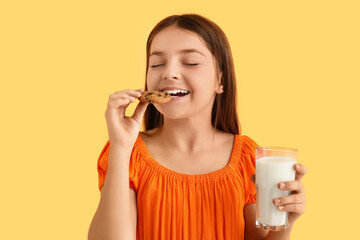 Little girl eating sweet chocolate cookie and drinking fresh milk on yellow background