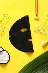Facial sheet mask with different cosmetic supplies, gypsophila flowers and leaf on yellow background