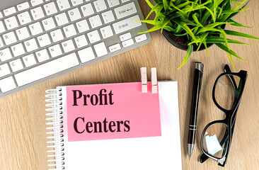 Profit centers text on pink sticky note attached to spiral notebook with pen, keyboard