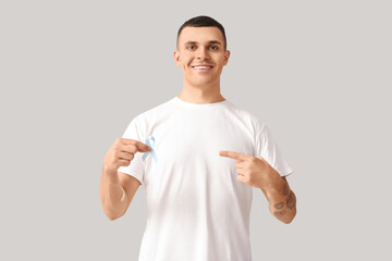 Handsome man pointing blue ribbon and medical patch on grey background. Prostate cancer concept
