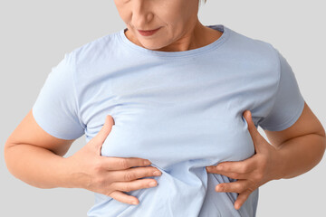 Mature woman checking her breast on light background, closeup. Cancer awareness concept