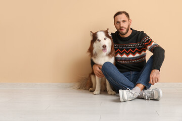 Handsome young man with cute Husky dog near beige wall