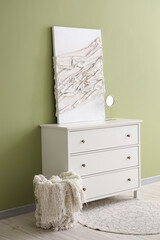 Modern chest of drawers with canvas and basket near green wall