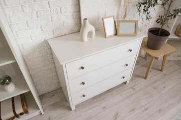 White commode with blank frames and decor in living room