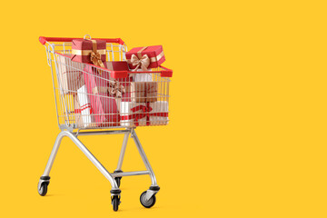 Shopping cart full of Christmas gift boxes on yellow background