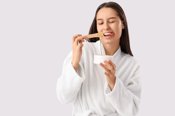 Beautiful young happy woman in bathrobe holding container with sugaring paste and spatula on grey background