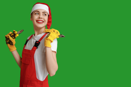 Young female construction worker in Santa hat with pliers on green background