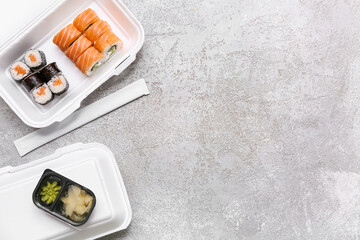 Plastic containers with tasty sushi rolls, marinated ginger and chopsticks on grey grunge background. Delivery concept