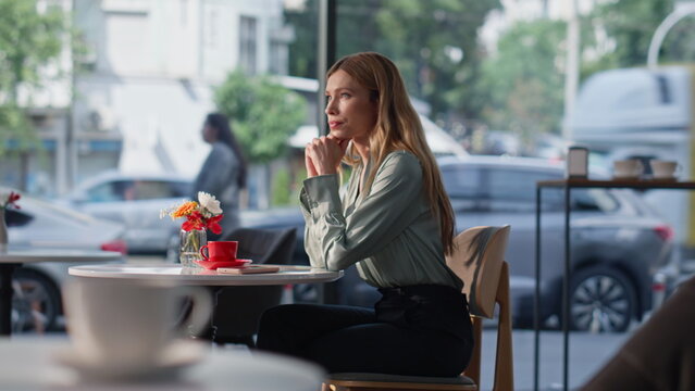 Lonely woman sitting cafe table with dreamy expression. Friendly waiter serving 