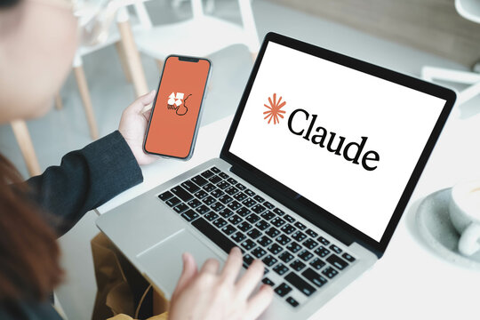 Bangkok, Thailand. June 13, 2025; Claude AI logo displayed on laptop screen while user holds smartphone with Anthropic splash screen at modern cafe table.