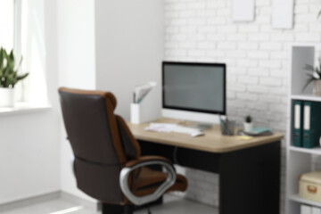 Interior of office with workplace, brown armchair, modern computer and shelving unit, blurred view