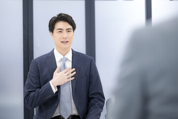 転職の面談や面接、昇進の面談などのビジネスイメージ　スーツを着た若い男性　自己アピールで説明する