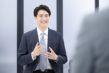 転職の面談や面接、昇進の面談などのビジネスイメージ　スーツを着た若い男性　自己アピールで説明する