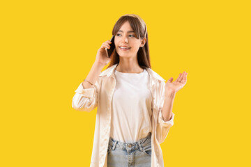 Beautiful young woman talking by mobile phone on yellow background