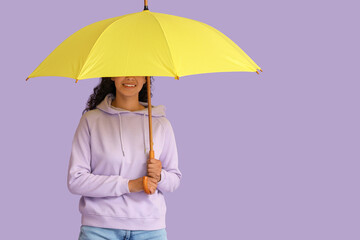 Happy young African-American woman with umbrella on lilac background