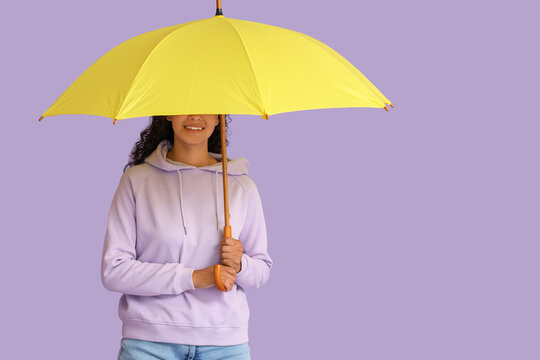 Fototapeta Happy young African-American woman with umbrella on lilac background