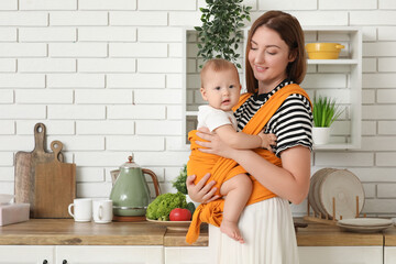 Happy young mother with little baby in sling in kitchen