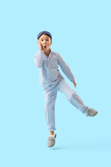 Shocked little boy in pajamas jumping on blue background
