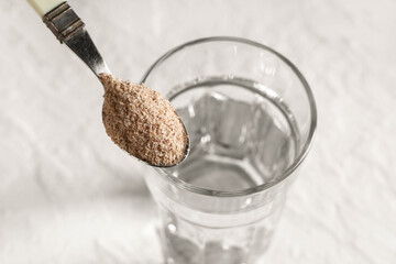 Glass of water and spoon with psyllium husk on white background, closeup