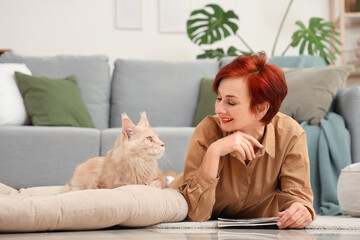 Mature redhead woman with cute Maine Coon cat lying on floor at home