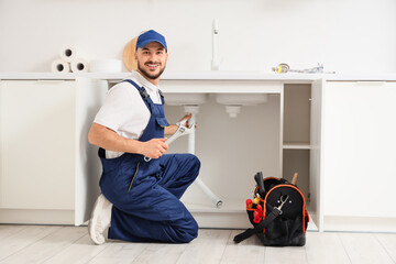 Male plumber with wrench and pipe in kitchen