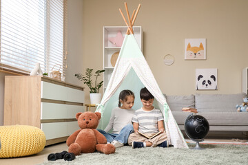 Cute children reading adventure book in play tent at home