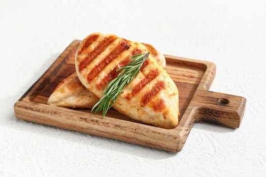 Wooden board with tasty grilled chicken breast and rosemary on white background