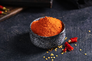 Bowl with red chili powder on black background