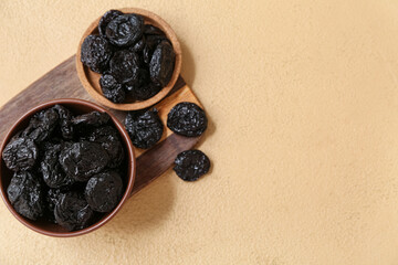 Bowls and wooden board with dried prunes on beige background