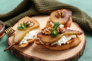 Wooden board of pear bruschetta with ricotta cheese and walnuts on green background, closeup