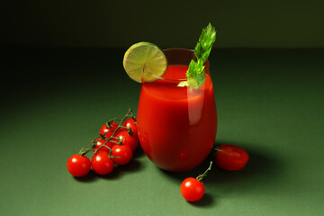 Glass of bloody mary with celery, lime slice and tomatoes on dark green background