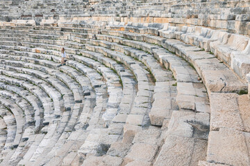 A young woman walk by ancient ruins in Patara, Turkey. Girl look at ruined amphitheater. History and adventure. This scenic archaeological site offers breathtaking view, perfect for cultural tourism.