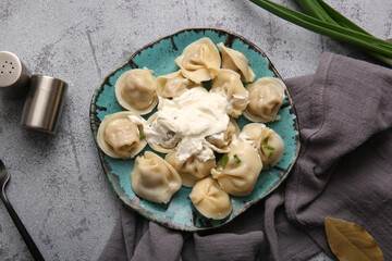 Plate of delicious boiled dumplings with sour cream and green onion on grey background
